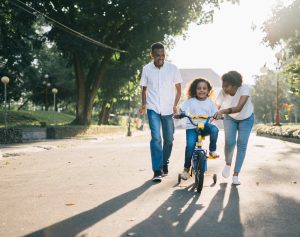 mom and dad in white shirts teaching child to ride a bike