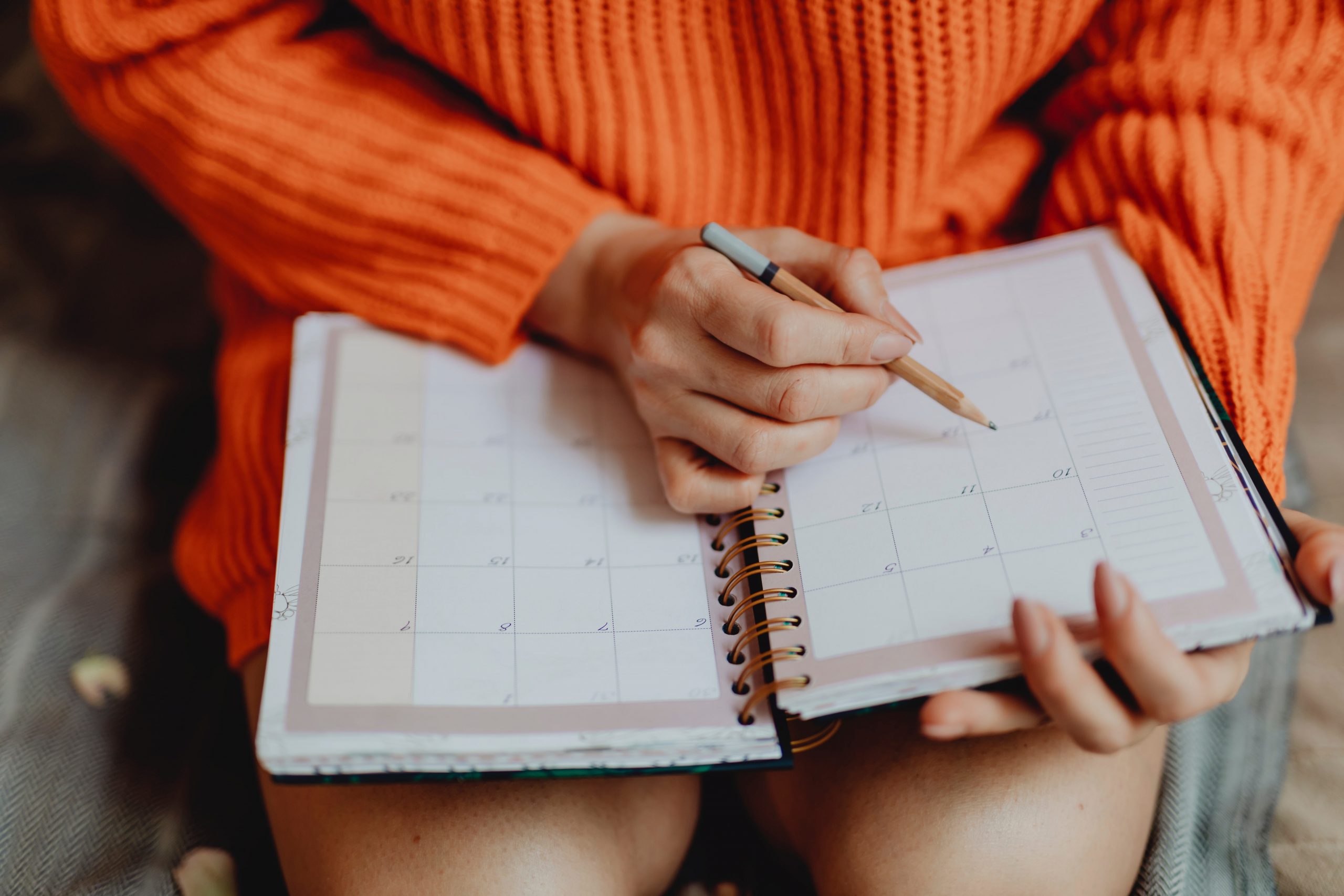 why calendars are important woman in orange sweater marking her calendar with a pencil