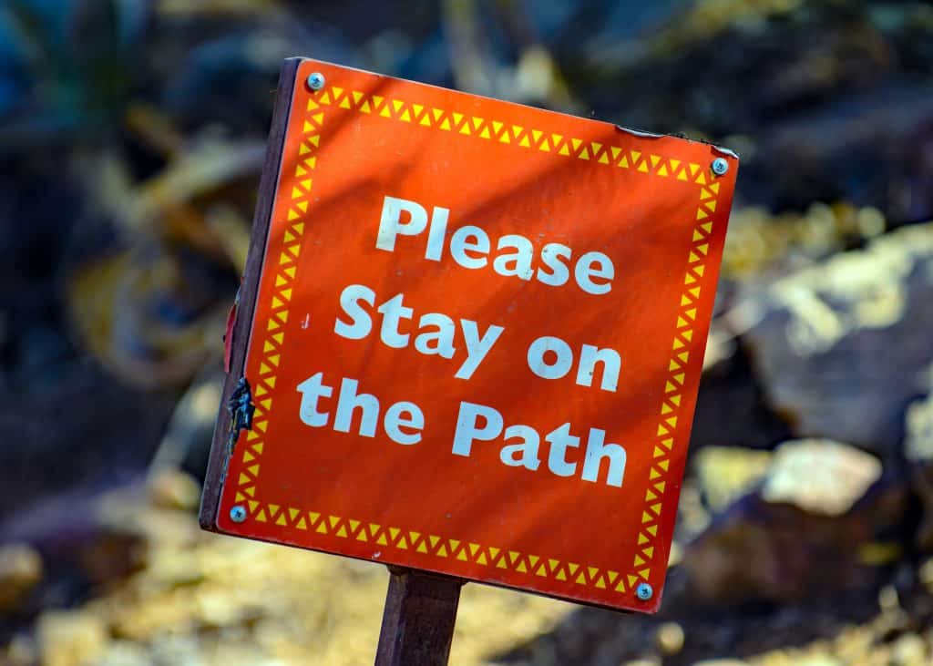 orange sign that says please stay on the path