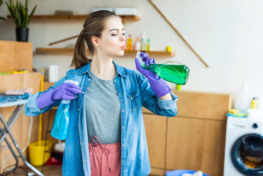 dark haired woman blowing the fake smoke off her cleaning bottles like she just shot a gun