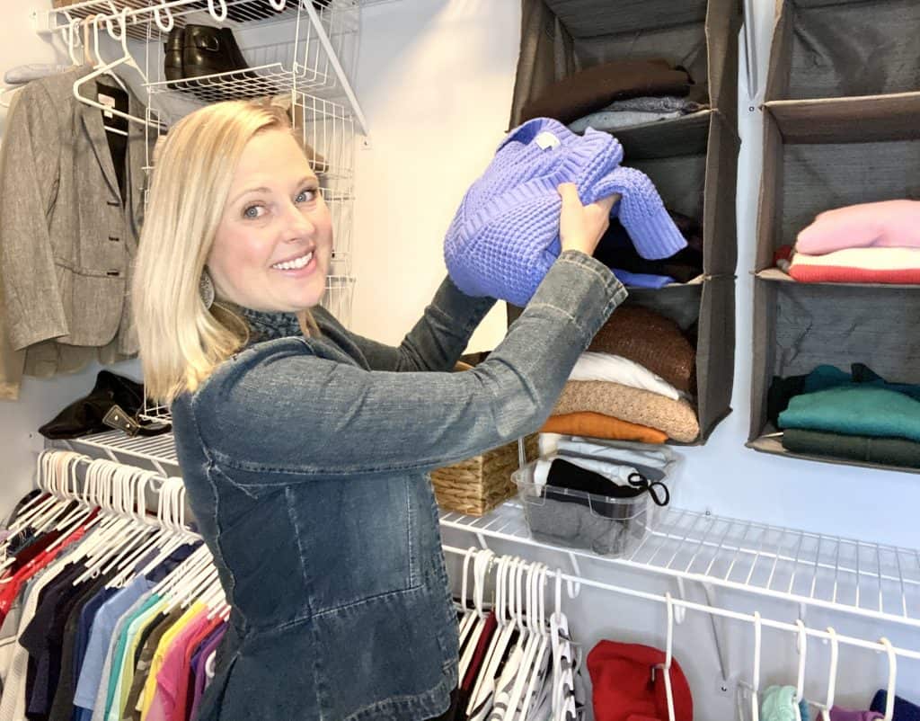 Julie Hazard putting away a blue sweater in an organized color coded closet