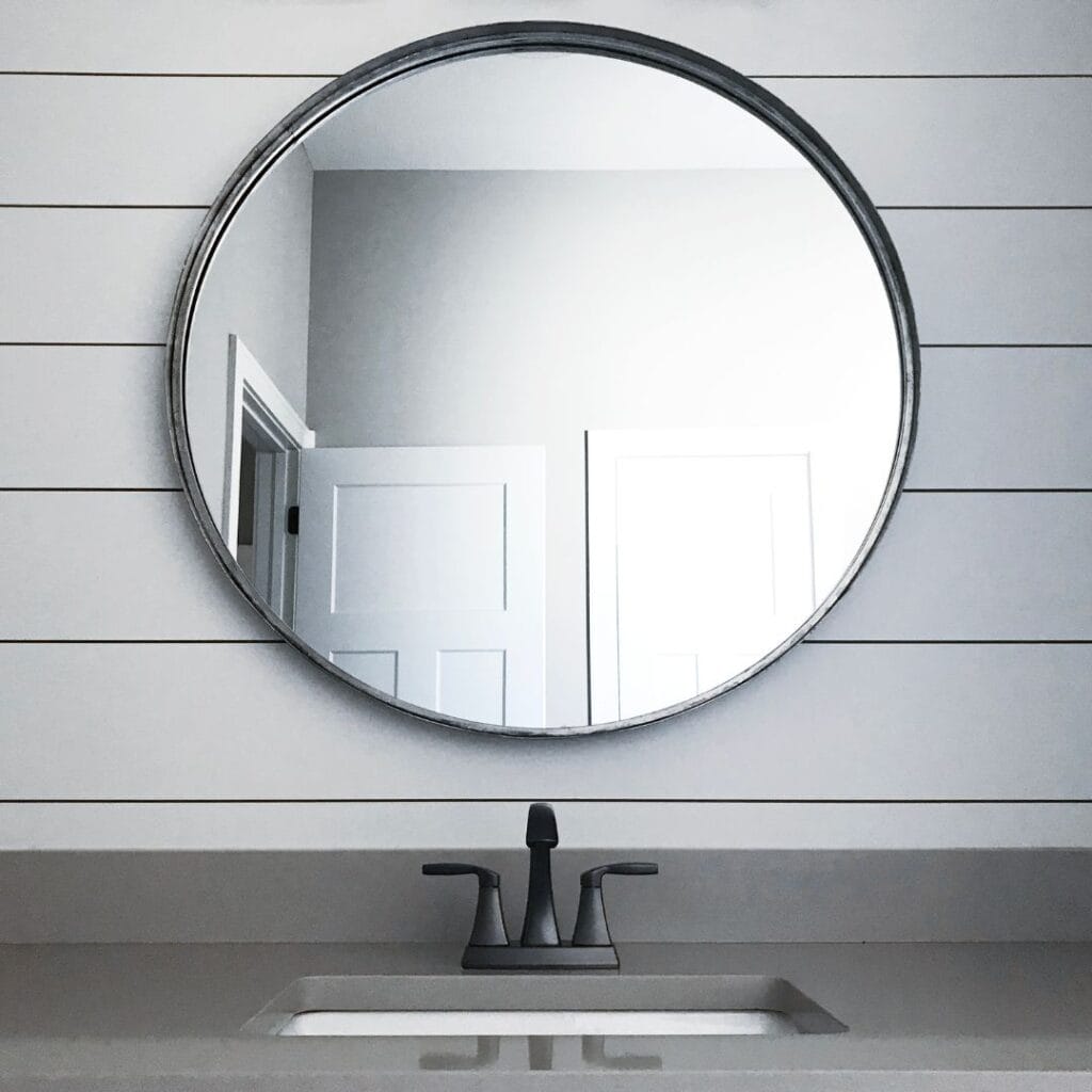 clean round mirror on shiplap wall above sink in grey countertop