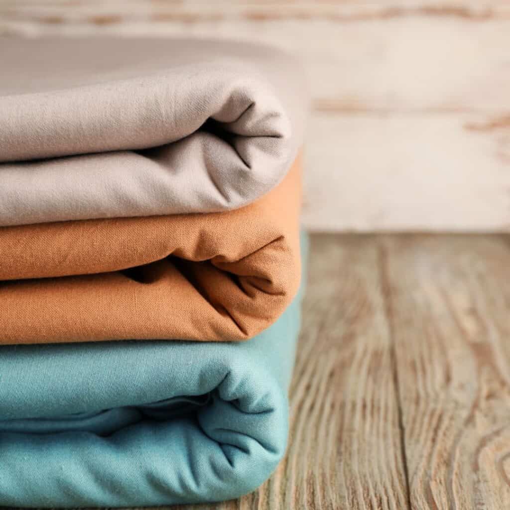 stack of folded sheets orange, blue and tan on a wood floor