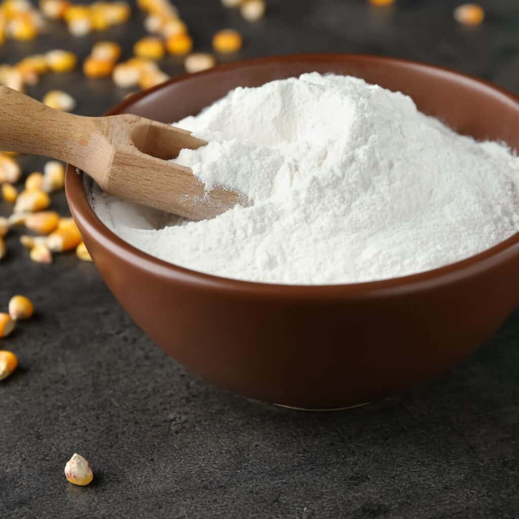 corn starch in a red bowl with yellow corn kernels on a dark table top