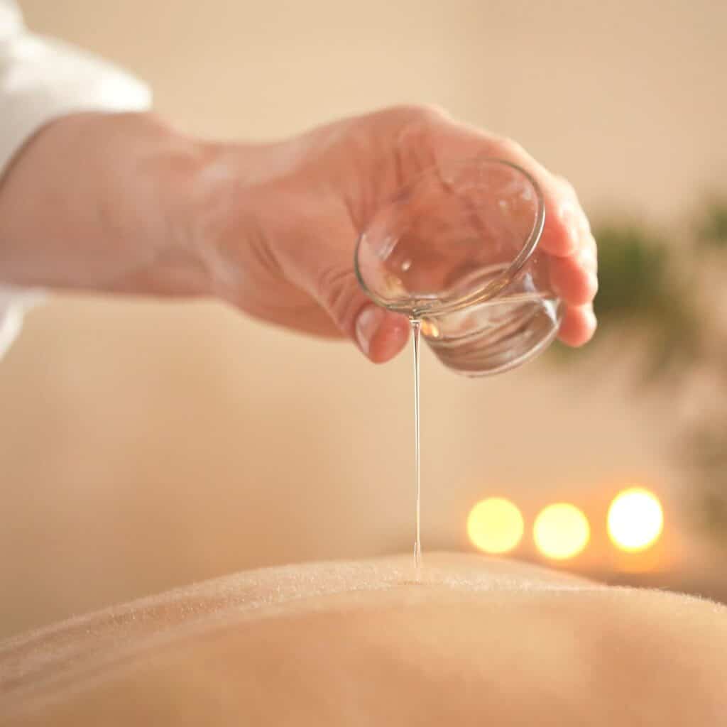 person pouring massage oil on someones back