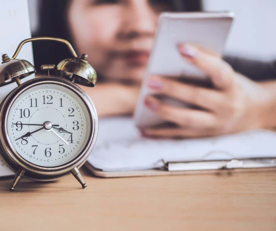 girl on her phone in the background next to a clock to show her wasting time