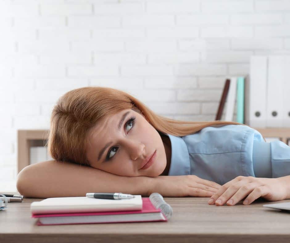 woman laying on her desk with notebooks in front of her and maybe wondering how to stop wasting time