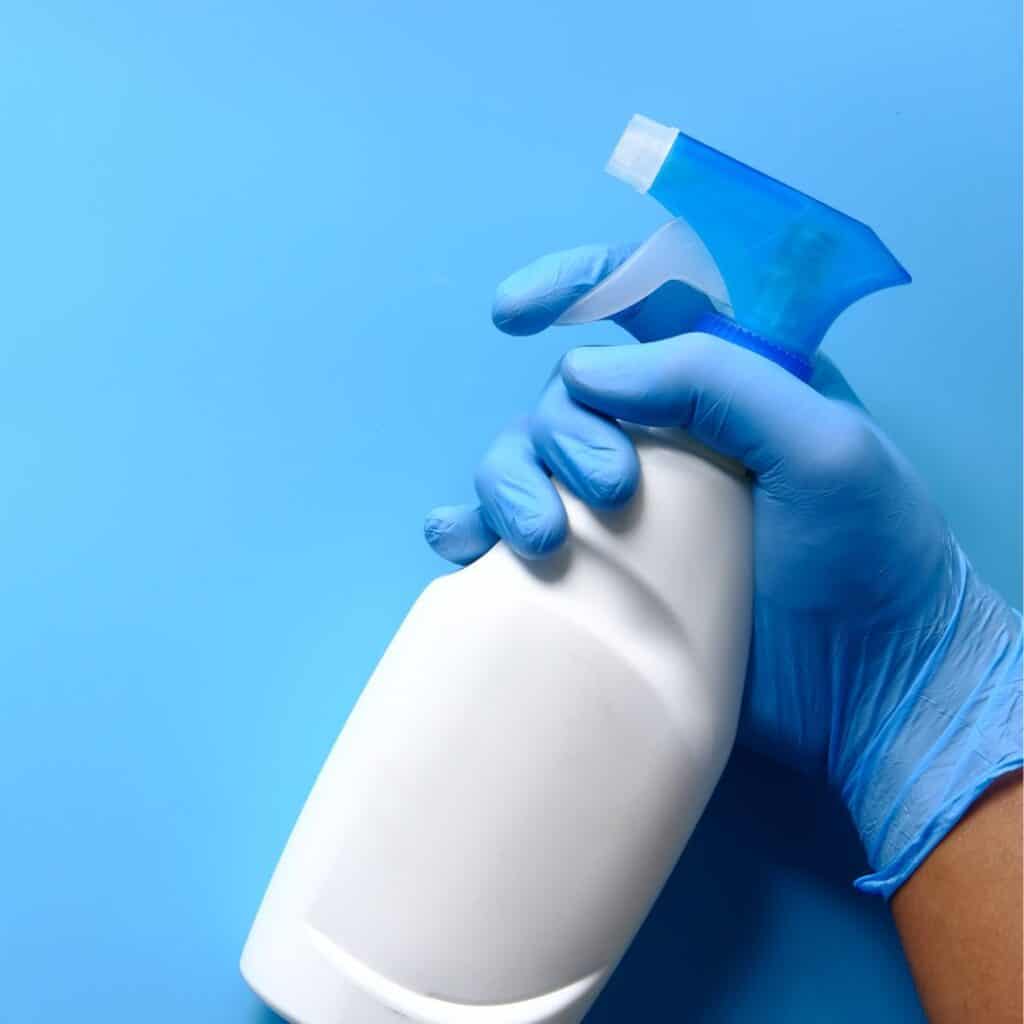 blue gloved hand holding white plastic spray bottle for how to clean a spray bottle post