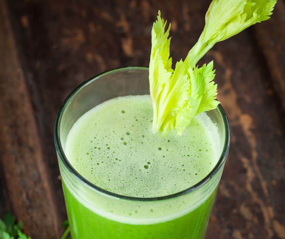 green celery juice in a clear glass with a stalk of leafy celery sticking out